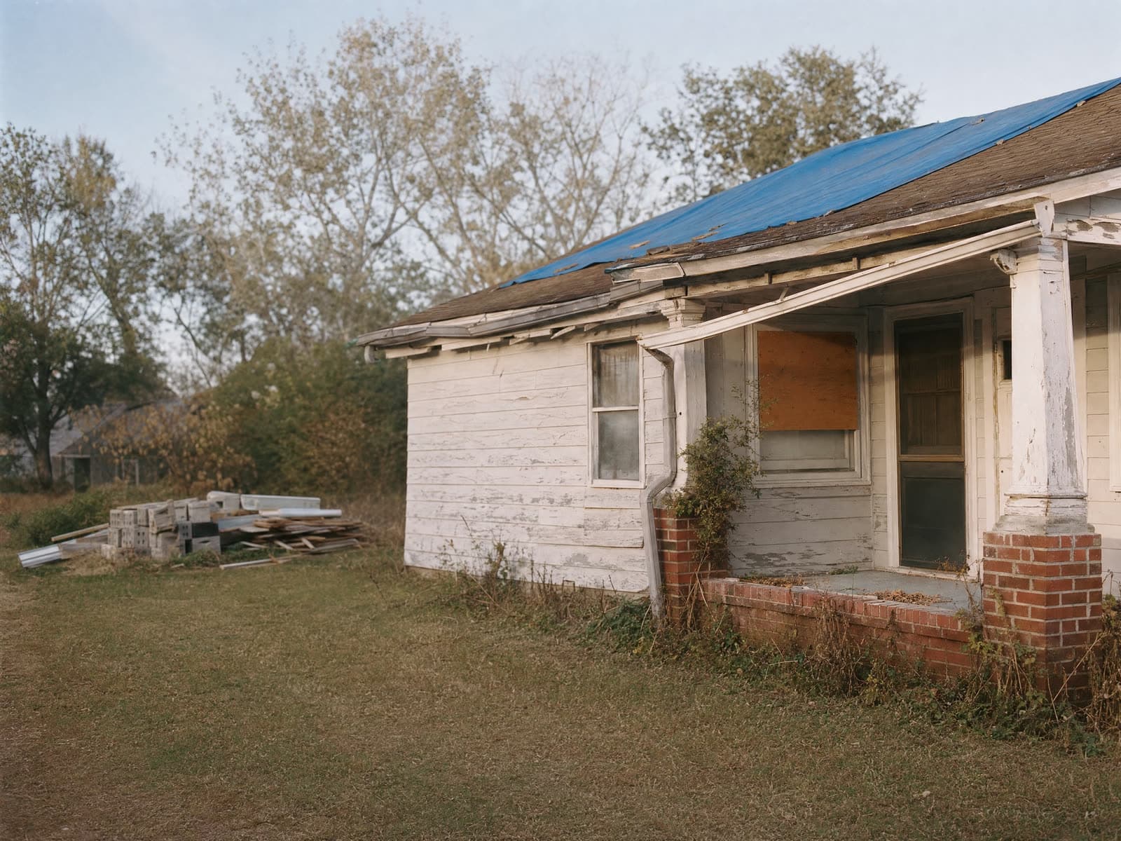 A worn older Hampton Roads house showing decades of deferred repairs, warm late light.